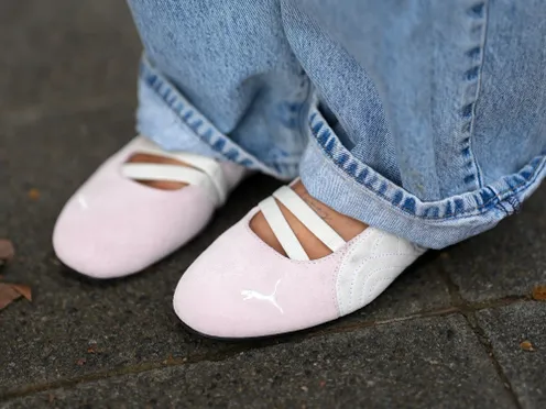 Person wearing ballet flats with crisscross elastic straps casual pants standing on a paved surface