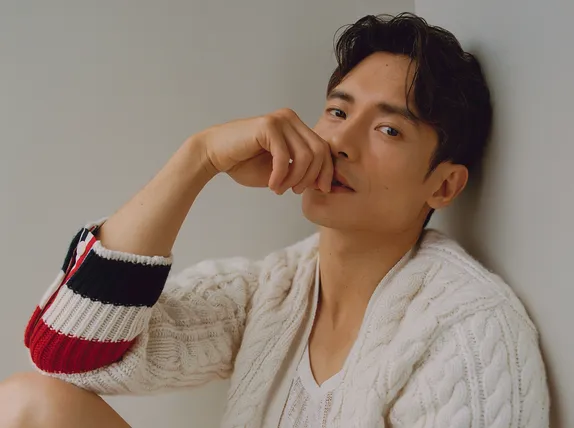 Manny Jacinto posing in a relaxed setting sitting against a wall