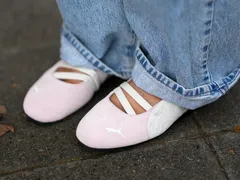 Person wearing ballet flats with crisscross elastic straps casual pants standing on a paved surface