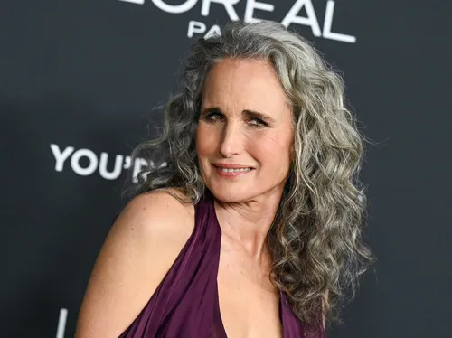 Andie MacDowell at a red carpet event smiling slightly with a branded backdrop behind